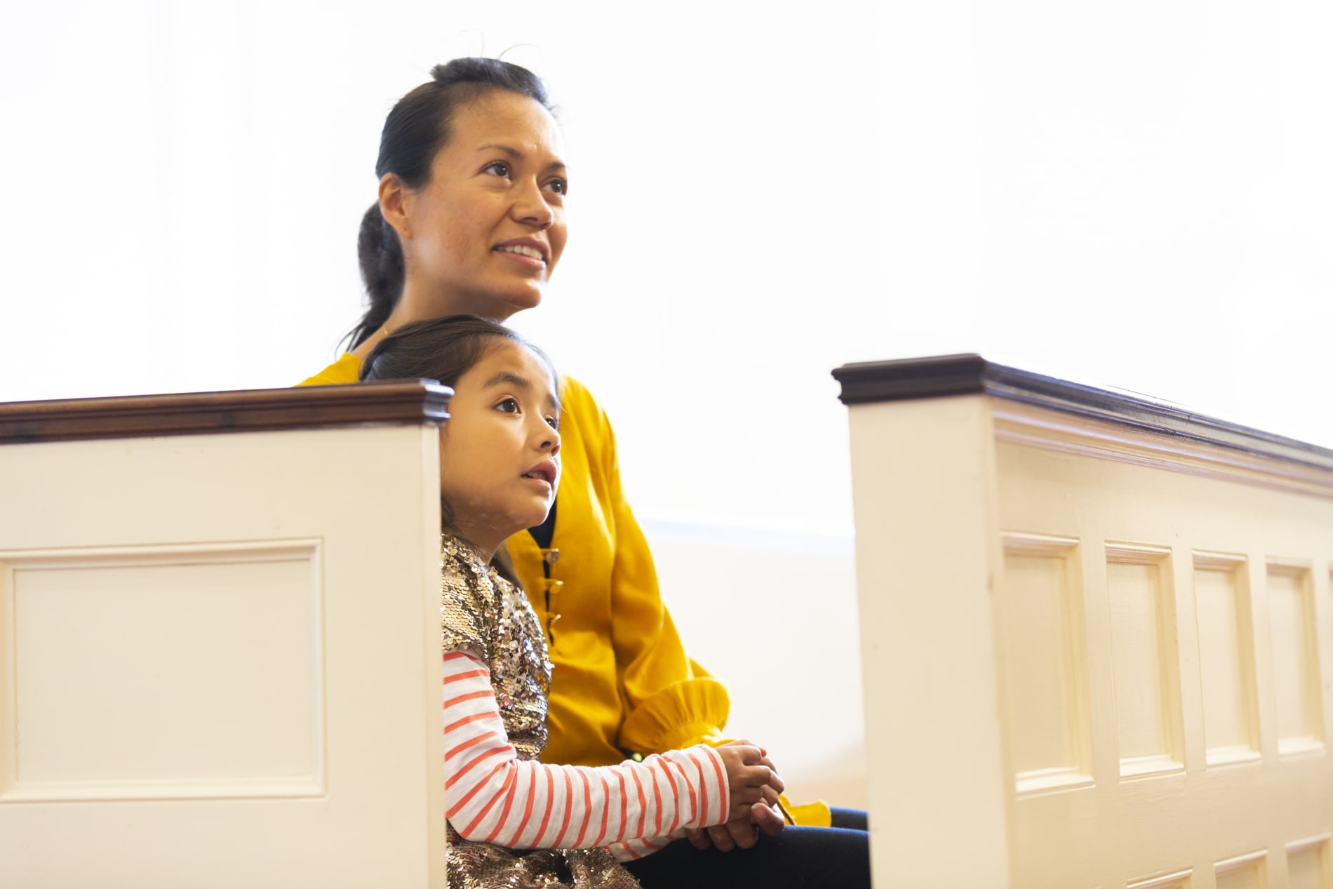A mother and her young daughter seated in a pew