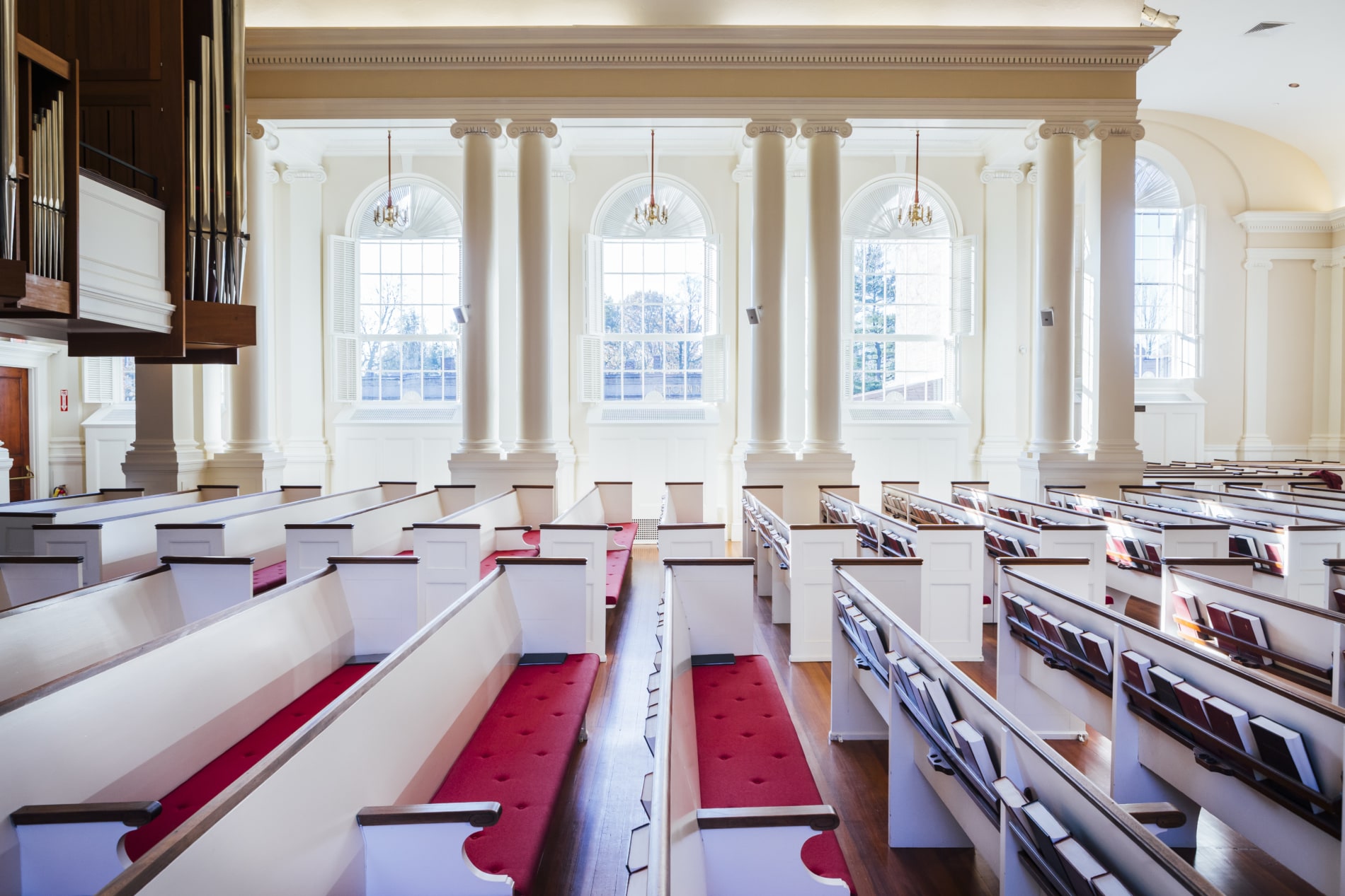 Interior of the sanctuary of Wellesley Village church showing pews, organ pipes, and clear glass windows.