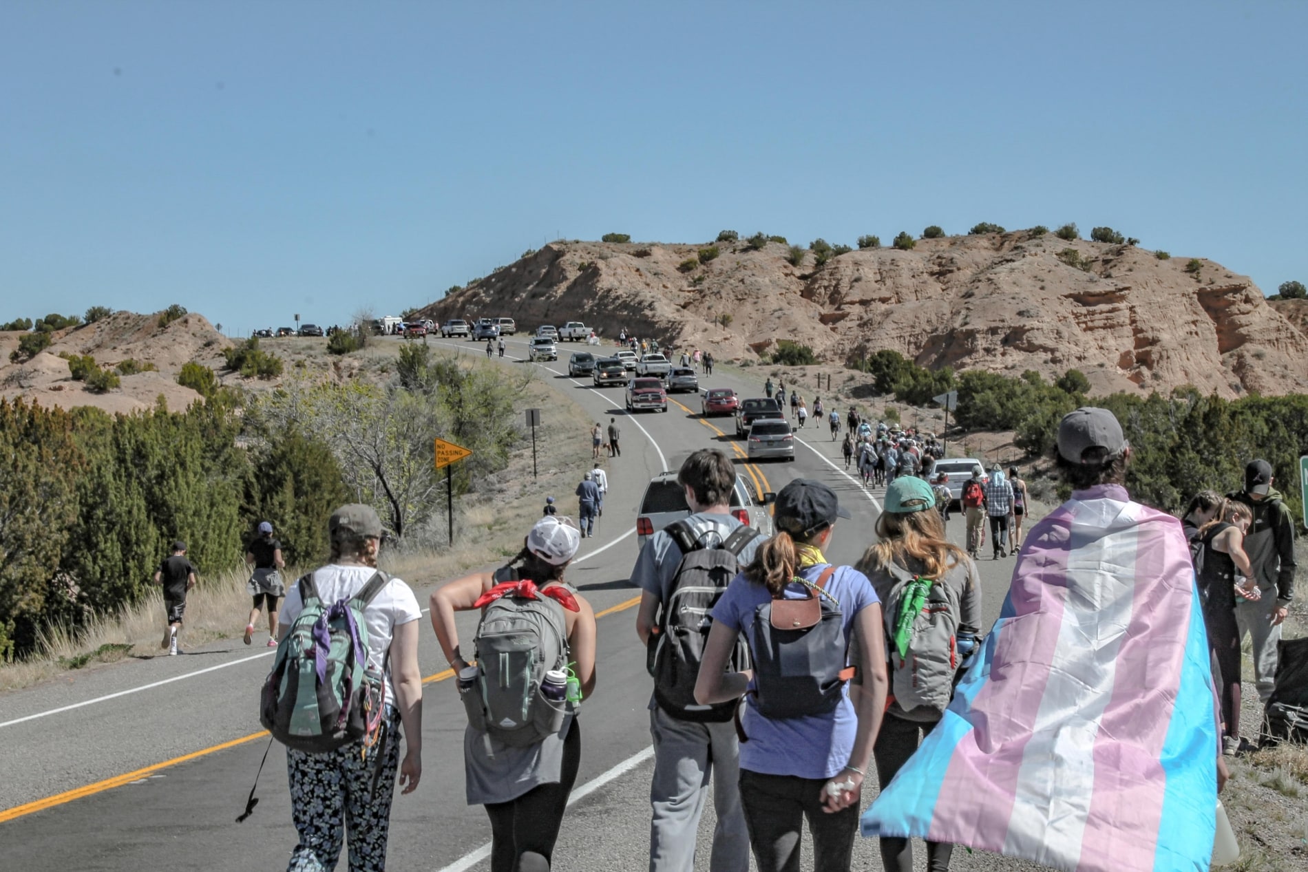 Church youth group travel up a road with a youth carrying flag of transgender symbol